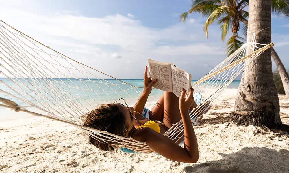 Ragazza che legge un libro coricata su un'amaca vista mare, Maldive | Eden Viaggi